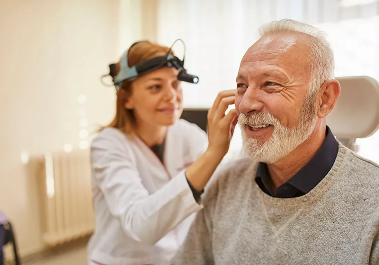 An elderly man is having his ears examined by an otolaryngologist.