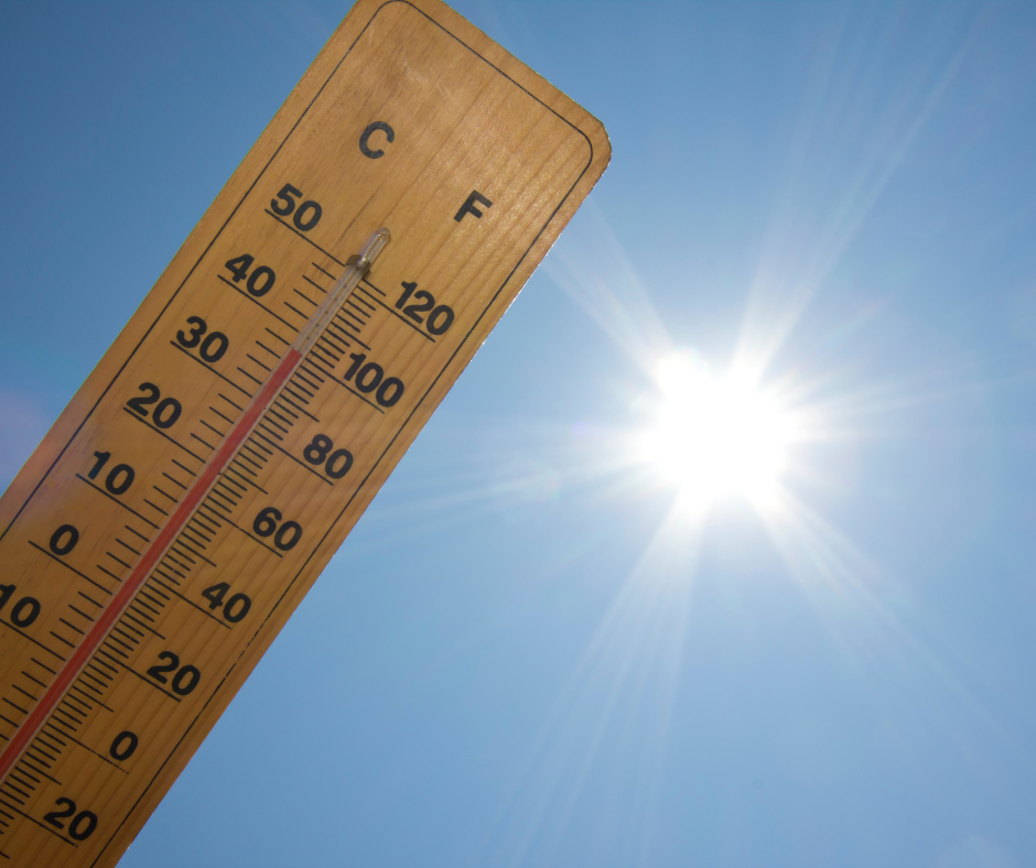A wooden thermometer shows a high temperature above 100°F against a bright, sunny, clear blue sky. Sun rays radiate outward, emphasizing the hot weather.