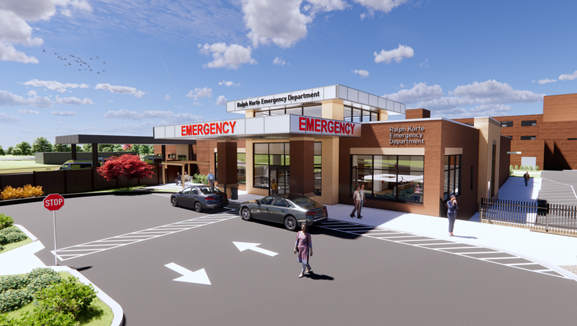 A modern hospital emergency department entrance with large red EMERGENCY signs, cars parked outside, people walking nearby, and a clear blue sky overhead.