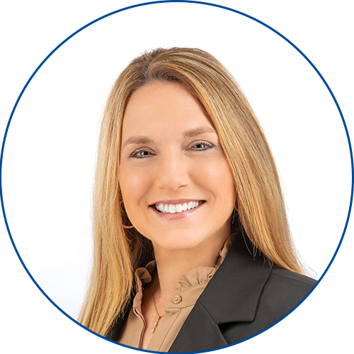Smiling woman with long, straight blonde hair, wearing a black blazer over a beige blouse, posed against a plain white background within a circular blue border.